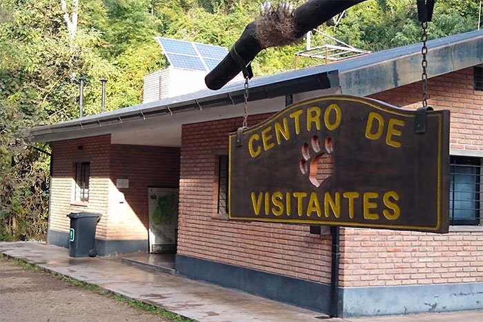 Cartel de madera del Centro de Visitantes del Parque Nacional Calilegua frente al edificio de ladrillo